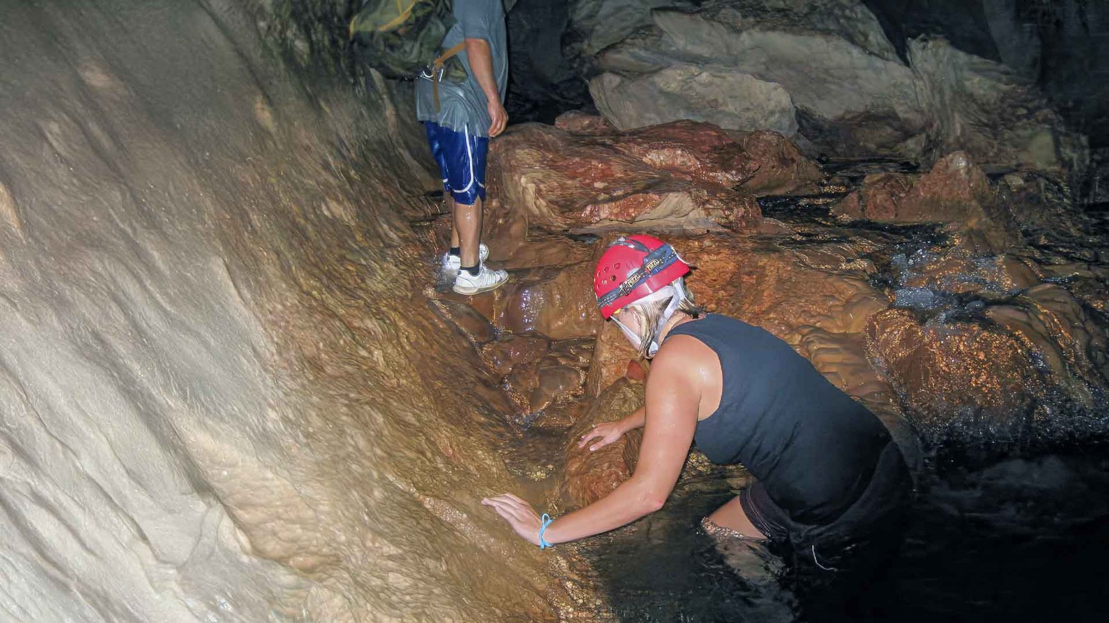 Couple exploring the Actun Tunichil Muknal tour cave chambers with helmets and headlamps during a guided adventure in Belize