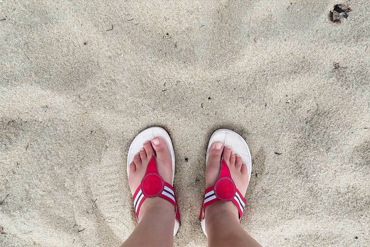 Close-up of two feet in red sandals resting on the white sand beaches of Belize — a relaxing moment from a Belize Family Adventure Travel Guide experience.