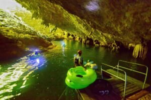 Group of adventurers with helmets and tubes ready to begin the cave tubing excursion at a jungle entrance during the Crystal Cave Expedition in Belize.