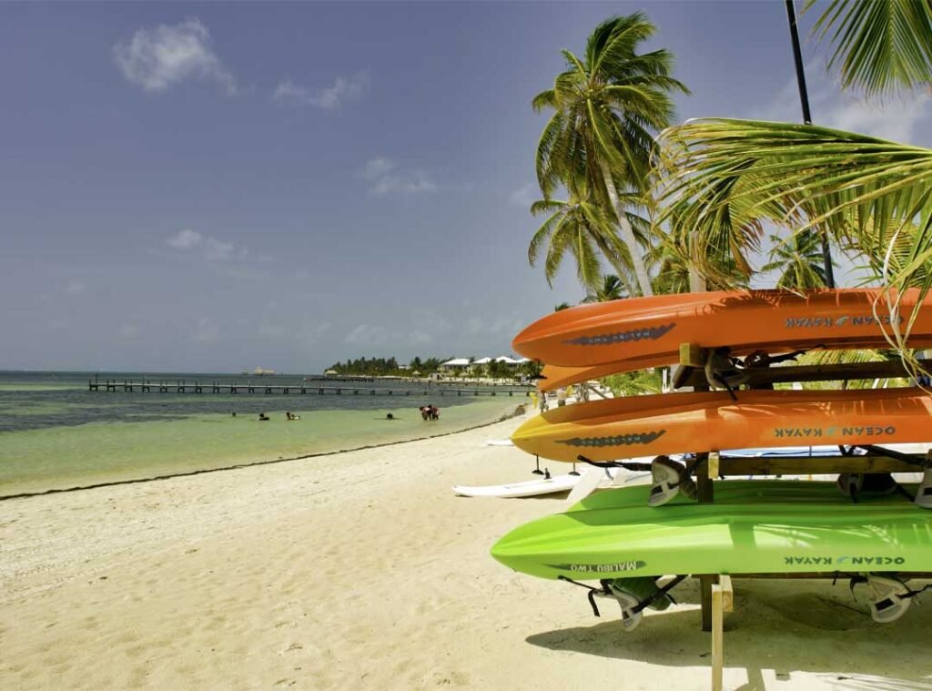 Kayak rentals lined up on the sandy beach in San Pedro, Ambergris Caye, Belize, with turquoise Caribbean waters in the background.
