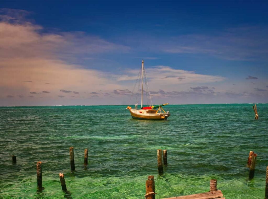 Sailboat at sunset near Caye Caulker Island, Belize, drifting between land and sea with vibrant skies reflecting the island’s tranquil, tropical charm.