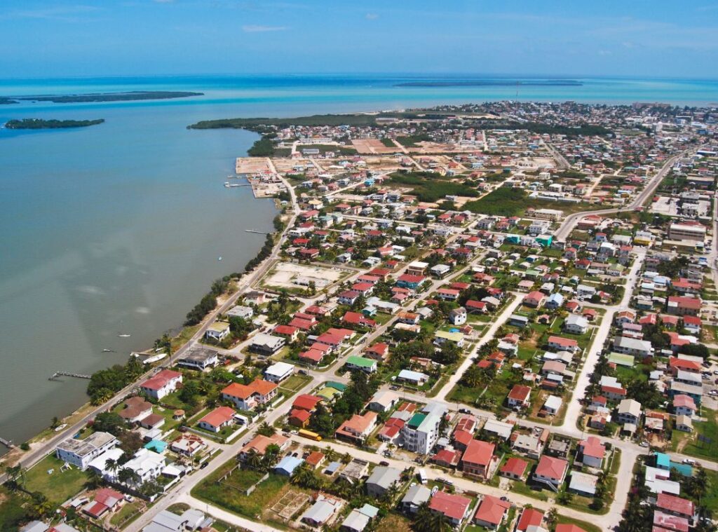 Aerial view of Belize City showing coastline, buildings, and waterways under a clear blue sky