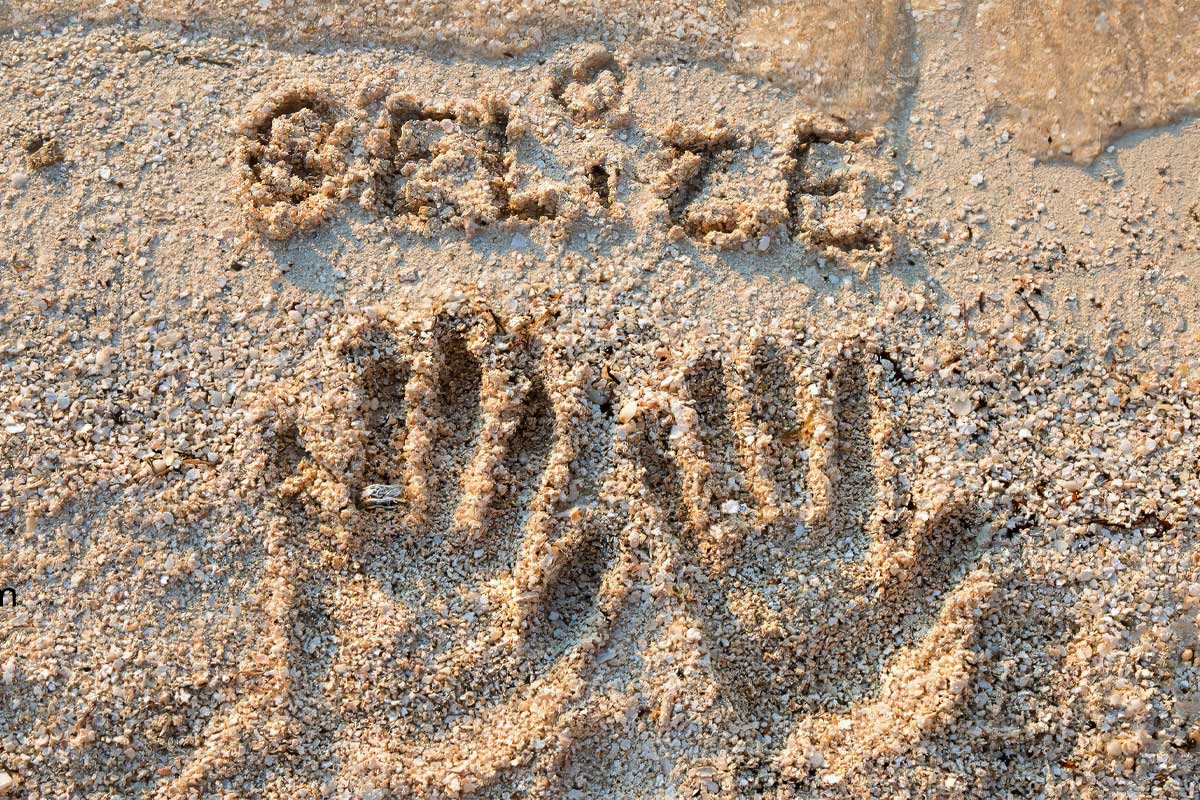 Handprints of a man and woman in the white sand on a tropical beach in Belize, symbolizing romance and connection — perfect for Belize vacation packages for couples.