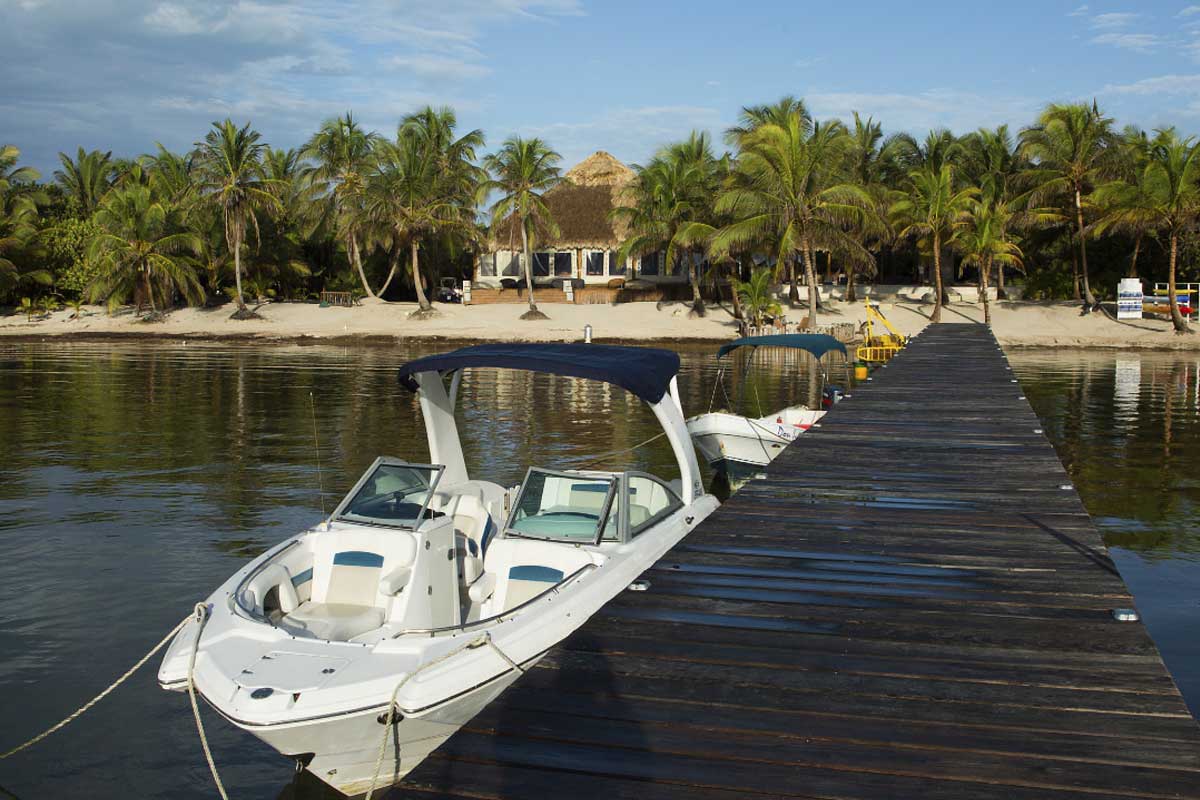 Secluded island with a private villa, coconut trees, white sand beach, and a luxury boat docked over turquoise waters — Belize vacation packages for couples