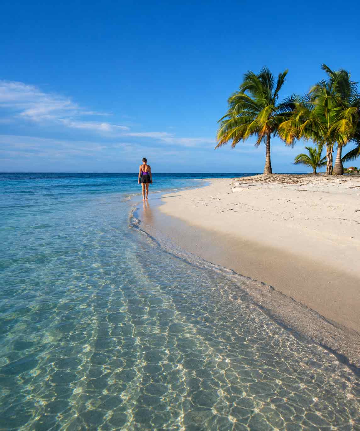 Belize-Atoll Woman walking along a secluded tropical beach during a Belize Sailing Vacations escape with crystal-clear Caribbean waters and palm trees in Belize.