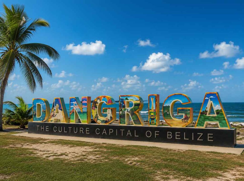 Colorful Dangriga Belize coastal sign reading “The Culture Capital of Belize” beside the Caribbean Sea with palm trees, tropical skies, and vibrant seaside scenery.