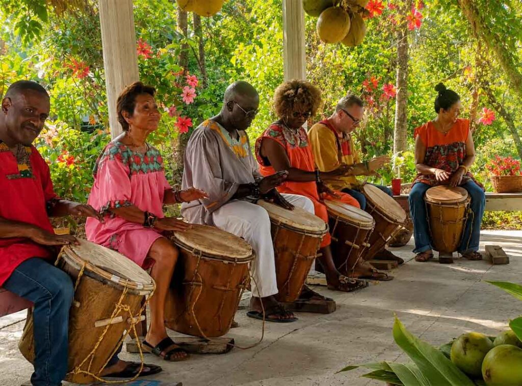 Visitors enjoying a traditional Garifuna drumming session in Hopkins Belize surrounded by tropical greenery, Caribbean culture, and vibrant community atmosphere.