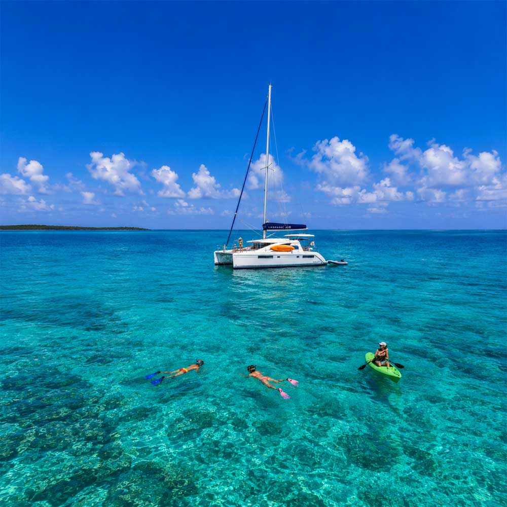 Belize sailing vacations with a luxury catamaran, snorkeling family, and kayaking adventure over the crystal-clear waters of the Belize Barrier Reef.