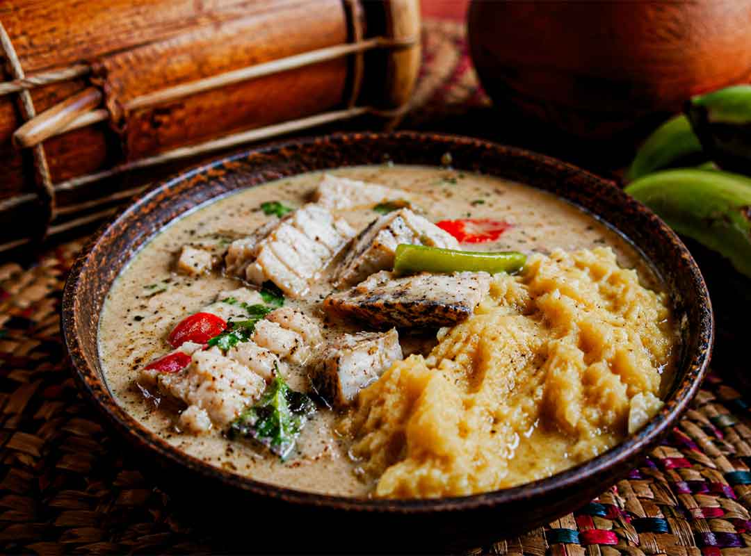 Traditional Garifuna hudut dish with coconut fish stew and mashed plantain served in a rustic bowl during a cultural Garifuna Drumming Workshop, Belize, surrounded by tropical textures and authentic Caribbean